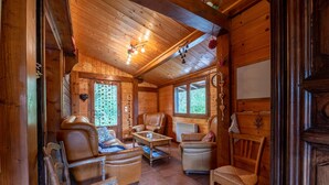 Ein gemütliches Holzhaus-Interieur mit Kamin, Ledersesseln, einem Couchtisch und einem großen Fenster.