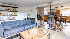 A modern living room with a blue sofa, a wooden coffee table, and a bookshelf. There is a kitchen area with a stove and dining space visible. - Les 5 Vallées - Appt en Duplex avec vue montagne (Briancon)