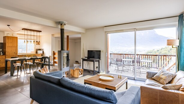 A modern living room with a sofa, coffee table, and a TV. There is a balcony with a table and chairs. - Les 5 Vallées - Appt en Duplex avec vue montagne (Briancon)