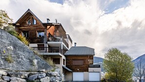 A multi-story wooden house with a garage, set against a mountainous backdrop. - Les 5 Vallées - Appt en Duplex avec vue montagne (Briancon)