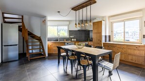 A modern kitchen with a wooden staircase, a dining table with chairs, and a view of the city through large windows. - Les 5 Vallées - Appt en Duplex avec vue montagne (Briancon)