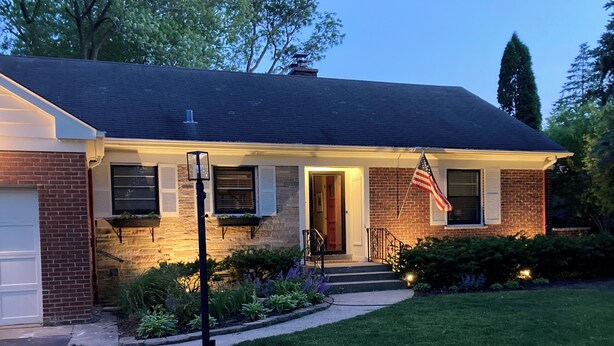 A two-story house with a brick facade, a front porch, and an American flag. - Charming light-filled 5-bedroom home (Wilmette)
