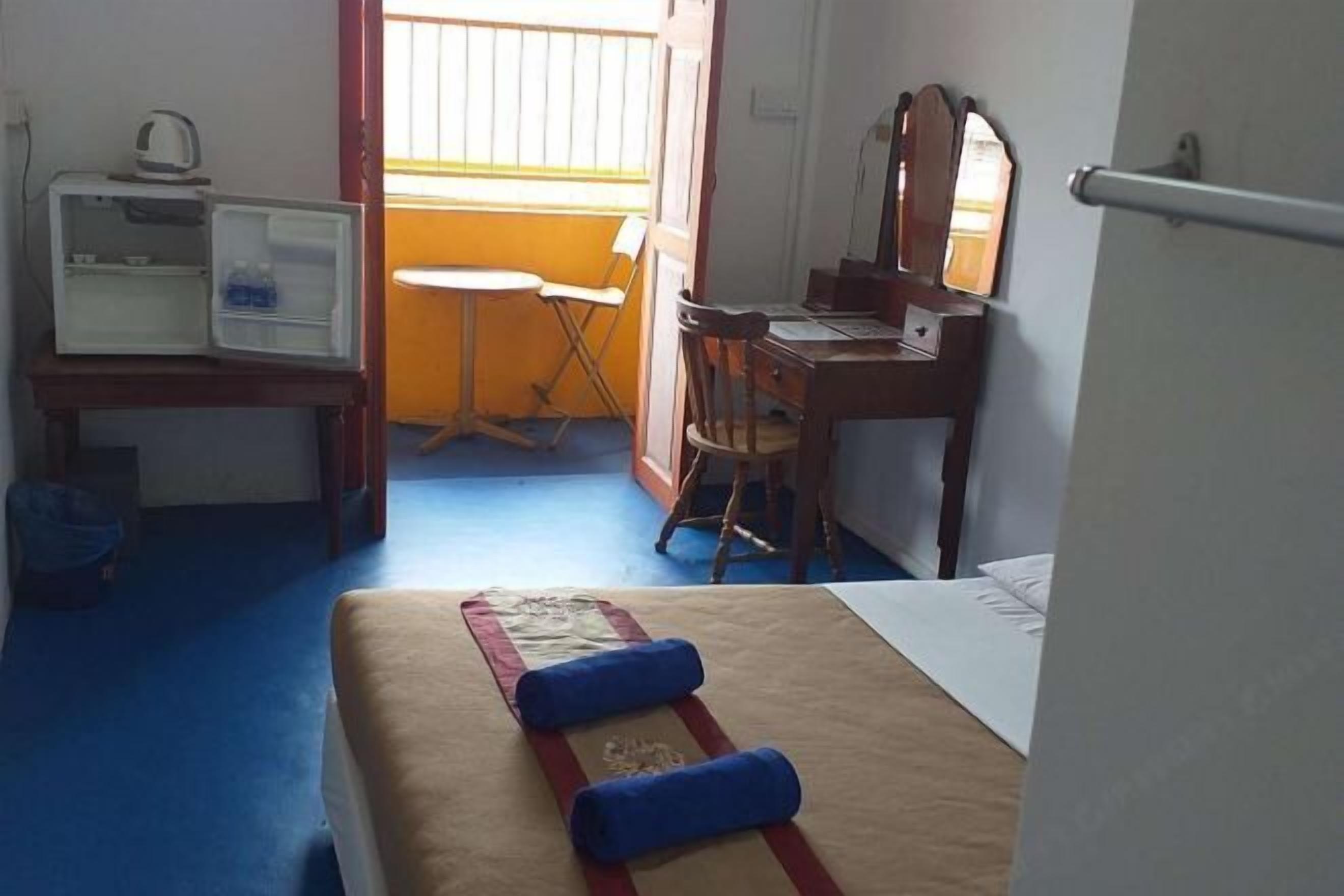 A hotel room with a bed, a desk, a chair, a small table, and a window with blinds.
