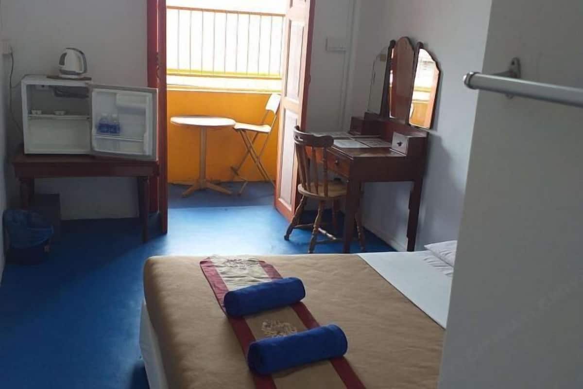 A hotel room with a bed, a desk, a chair, a small table, and a window with blinds.