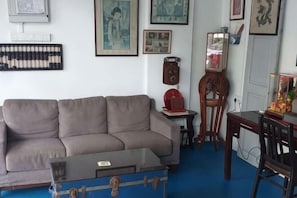 Un salon comprenant un canapé, une table basse, une chaise en bois, une petite table avec une horloge et des tableaux encadrés accrochés au mur.