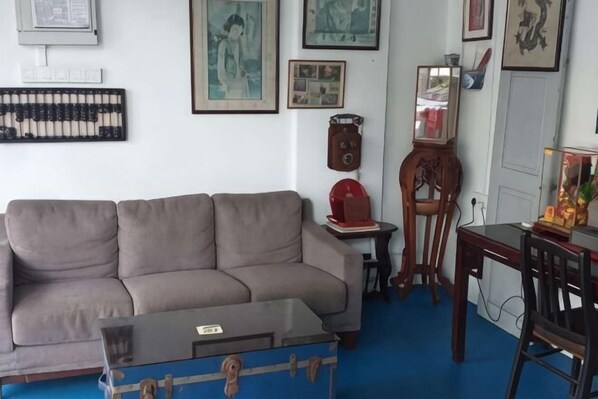 A living room with a sofa, a coffee table, a wooden chair, a small table with a clock, and framed pictures on the wall. - D Riverside Inn (Melaka)