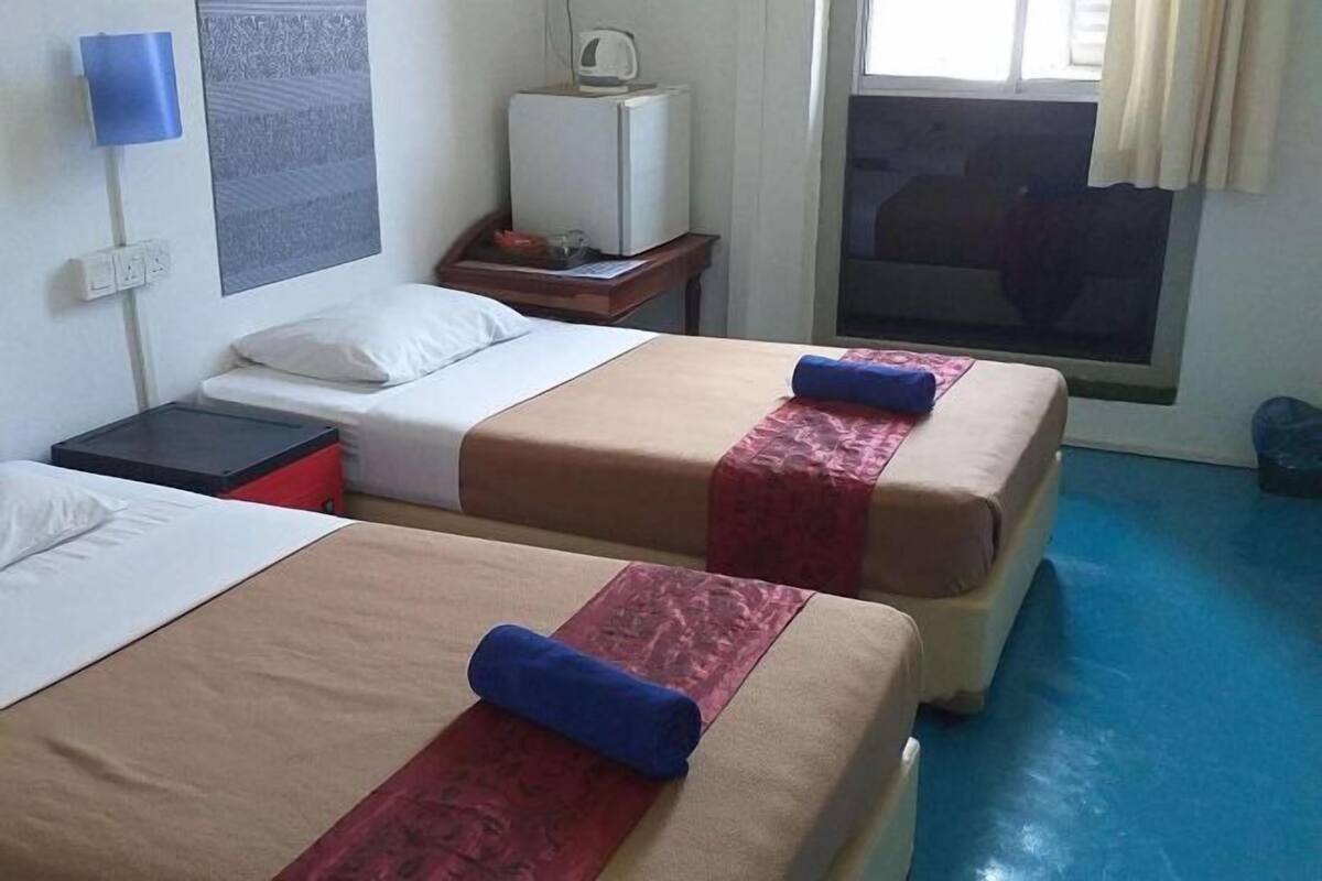 A hotel room with two beds, a small desk, a television, and a window with curtains.