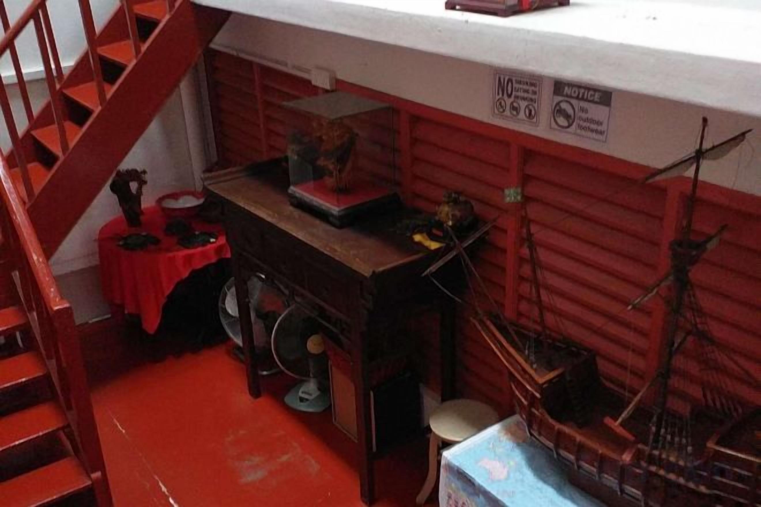 Une pièce avec un escalier rouge, une petite table sur laquelle se trouvent divers objets, et une maquette de bateau.