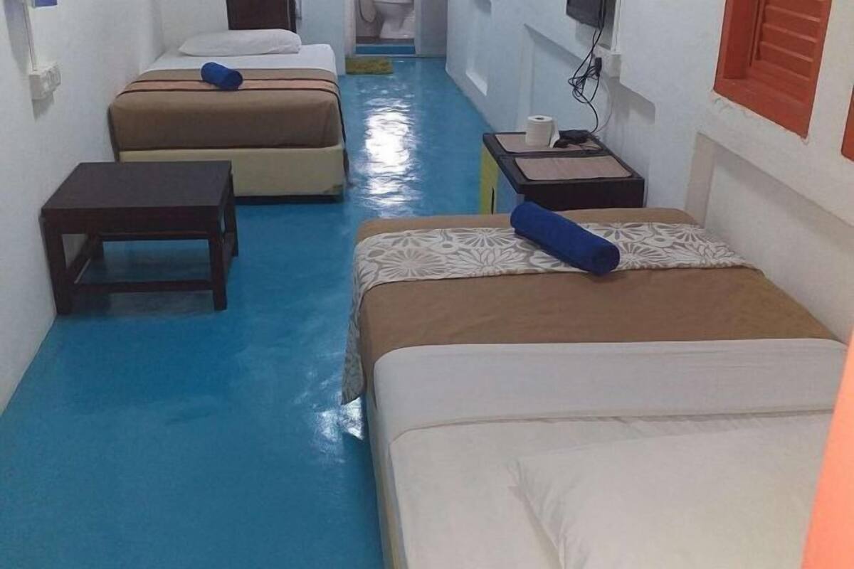 A hotel room with two beds, a small table, a nightstand, and a bathroom visible in the background.