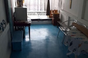 Una habitación pequeña con escritorio, una silla, una cama con colcha estampada y una ventana con cortinas.