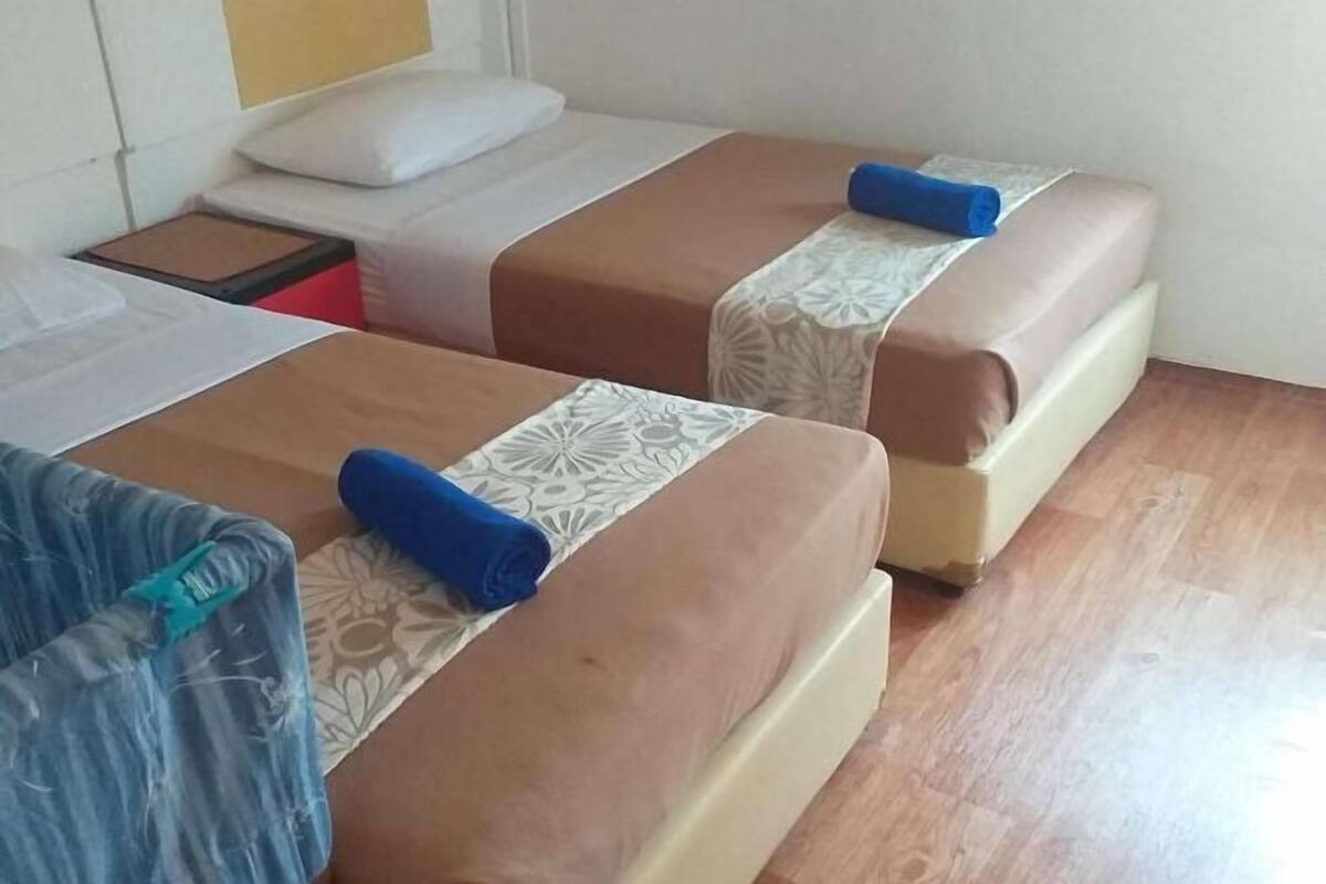 A hotel room with two beds, each with a patterned bedspread and a blue pillow.