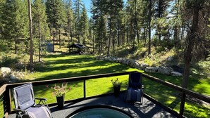 A hot tub with two lounge chairs, a stone wall, and a view of a forested area with a gazebo.