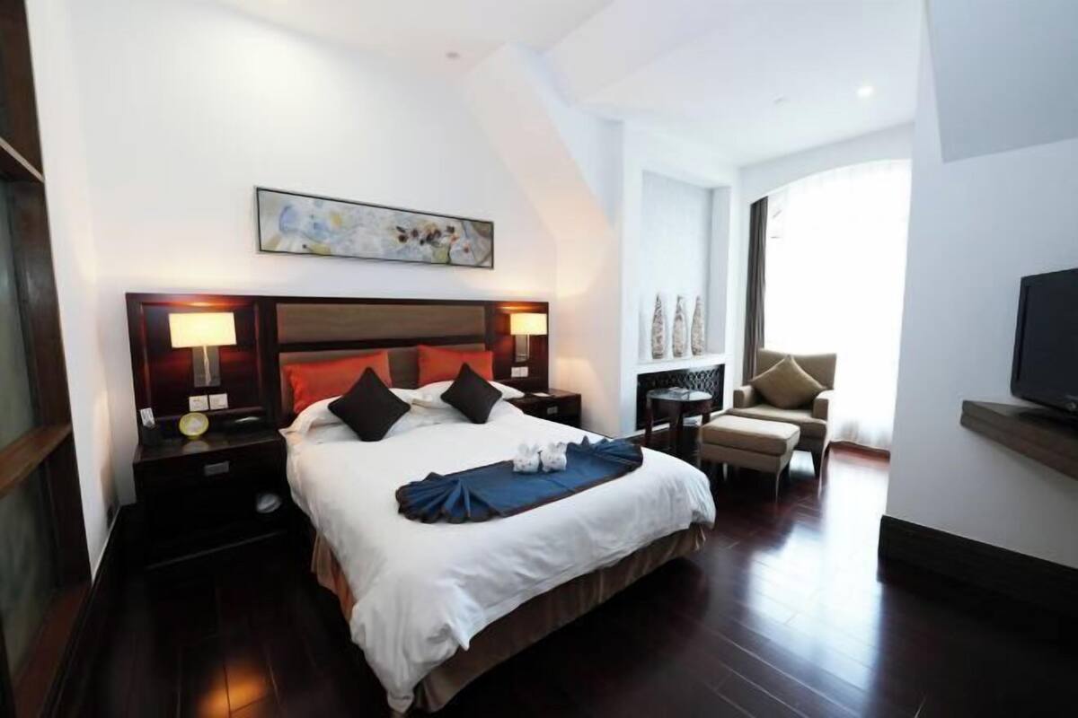 A hotel room with a large bed, bedside tables with lamps, a television, and a chair.