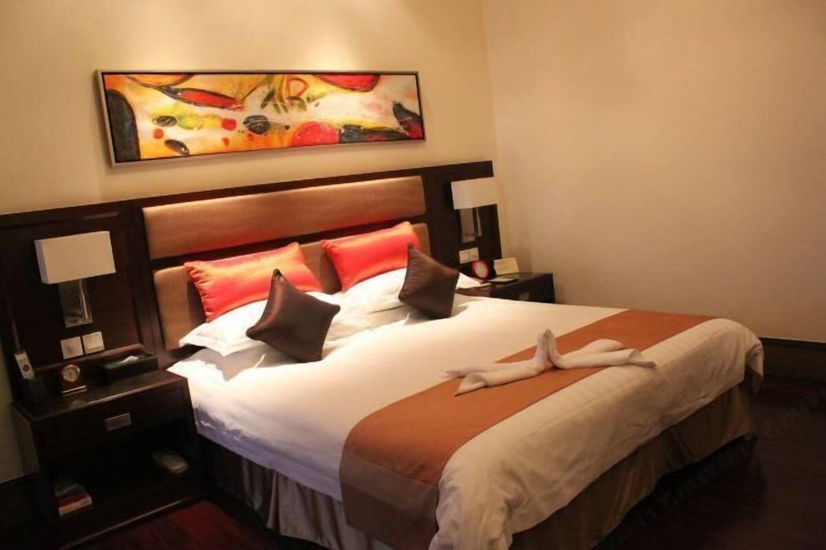 A hotel room with a bed, nightstands, a painting, and a towel on the bed.