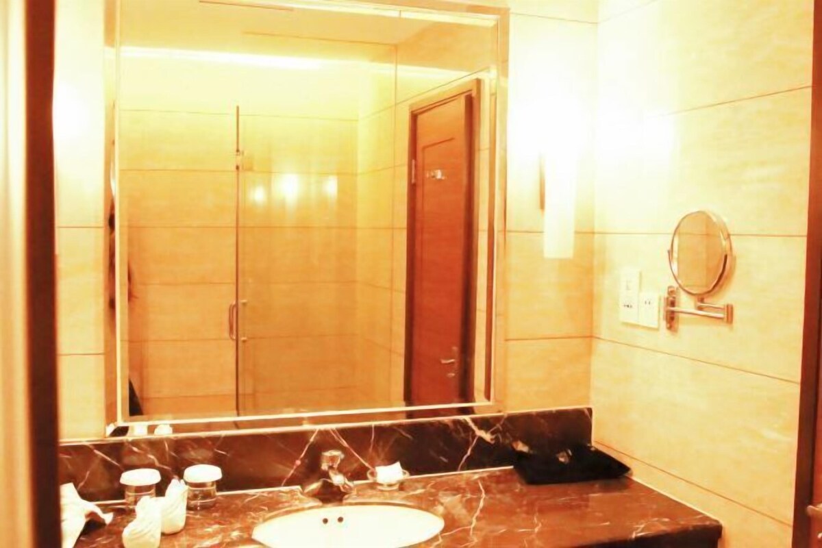Une salle de bain avec un lavabo en marbre, un grand miroir et une porte en bois à l’arrière-plan.