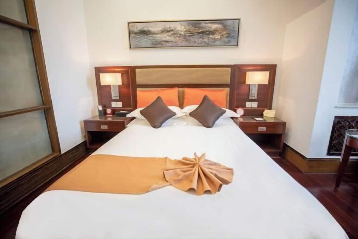 A hotel room with a large bed, two bedside tables, a headboard, and a painting on the wall.