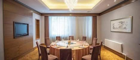 A conference room with a round table, chairs, a chandelier, a television, and a framed picture on the wall.