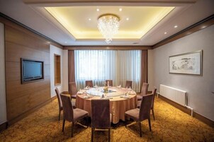 Un salón de conferencias con una mesa redonda, sillas, una araña, una televisión y un cuadro en la pared.