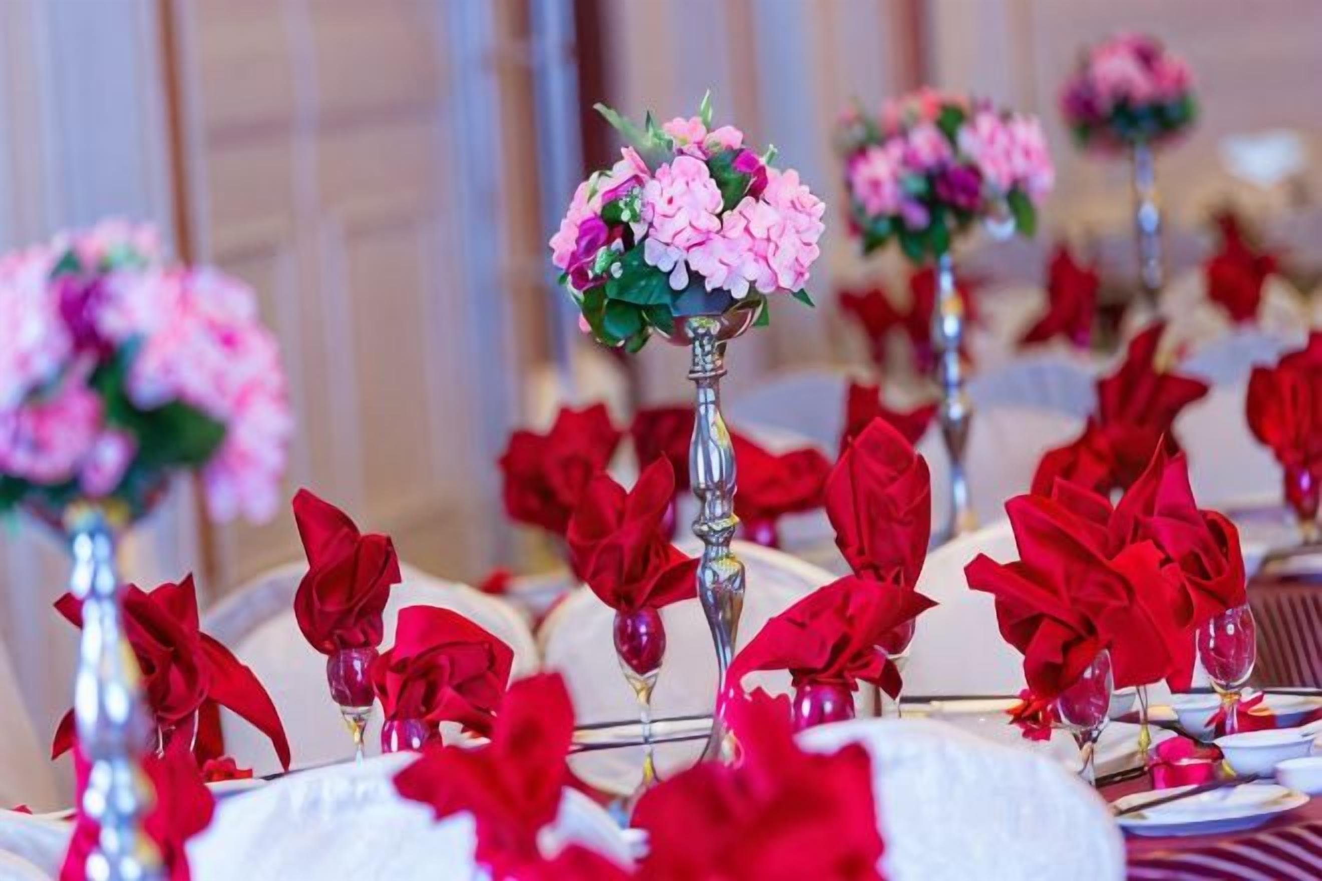 A table set with red napkins and a centerpiece with pink flowers.
