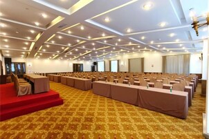Un salón de conferencias con filas de mesas, un escenario y piso alfombrado.