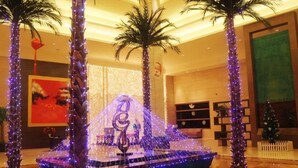 Un hall d’entrée agrémenté d’un piano, de palmiers et d’un sapin de Noël.