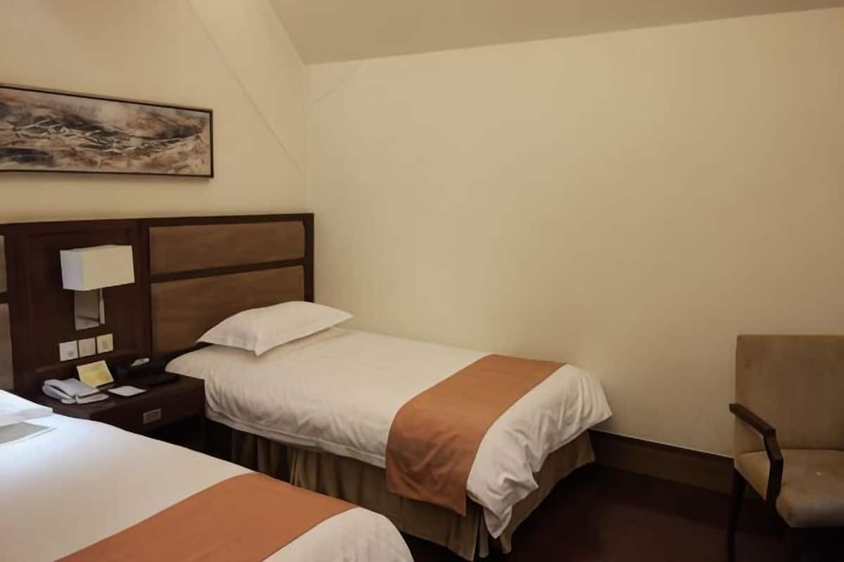 A hotel room with two beds, a nightstand with a lamp, a chair, and a painting on the wall.