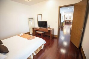 A hotel room with a bed, a desk with a television, and a door leading to a hallway. - Mohe Peak Yuezhiyue Hotel (Mohe)