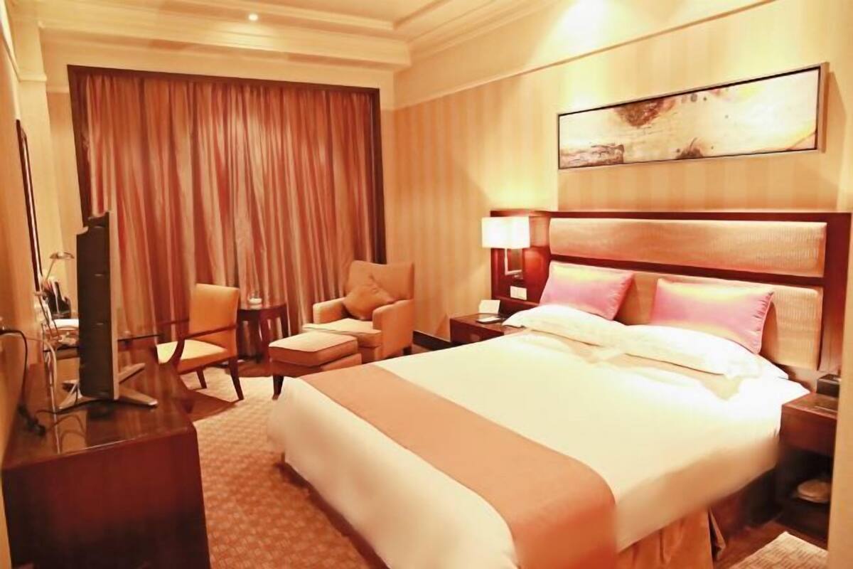 A hotel room with a large bed, a desk, a chair, a TV, and a curtain.
