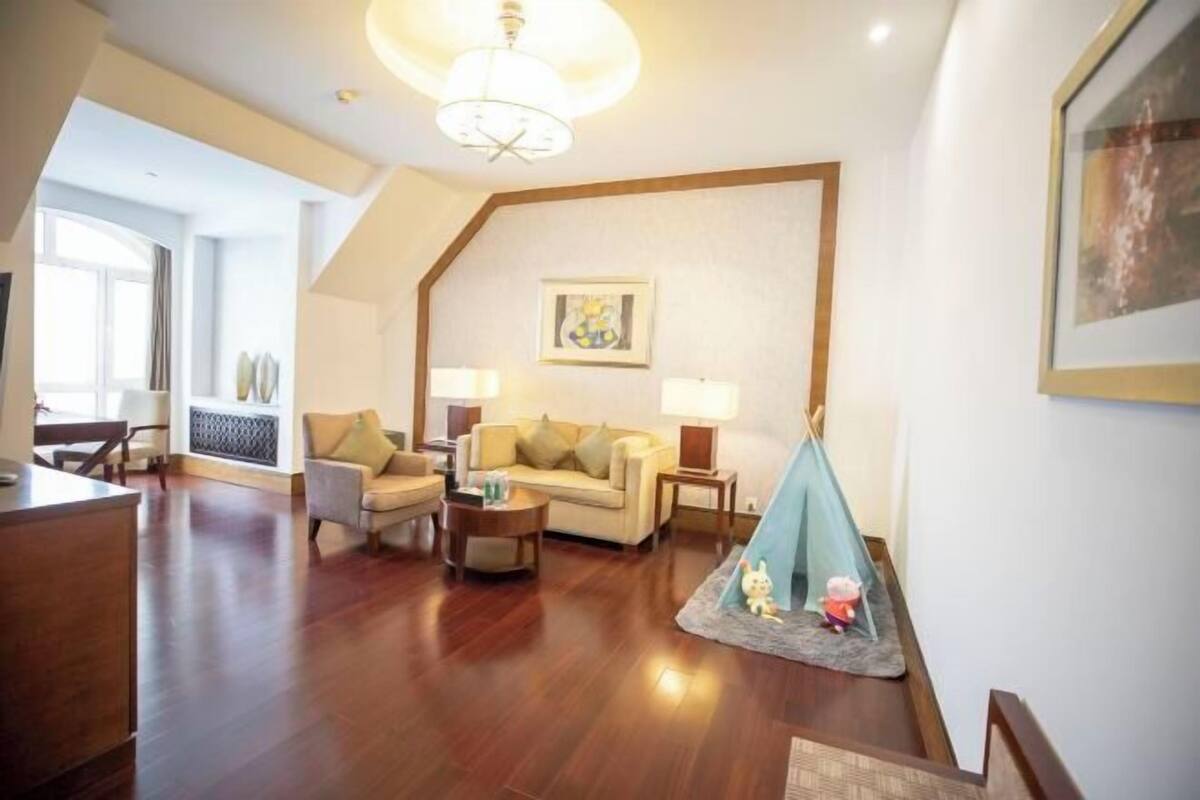 A living room with a sofa, armchairs, a coffee table, a lamp, a painting, and a tent.