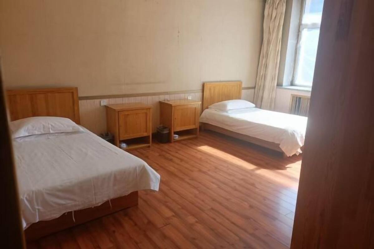 A room with two beds, wooden headboards, a small wooden cabinet, and a radiator.