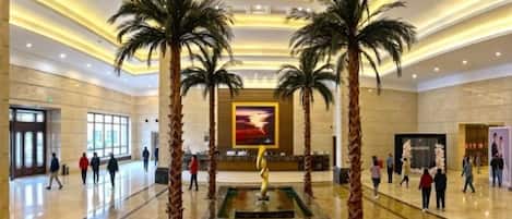 A spacious lobby with a fountain, palm trees, and a large painting on the wall.