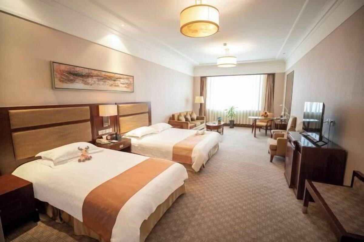 A hotel room with two beds, a desk, a TV, and a window with curtains.