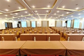 Une salle de conférence avec des rangées de tables et de chaises, équipée de microphones et de bouteilles d’eau.