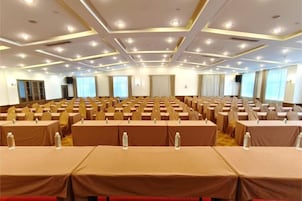 Un salón de conferencias con mesas y sillas dispuestas en filas, equipado con micrófonos y botellas de agua.