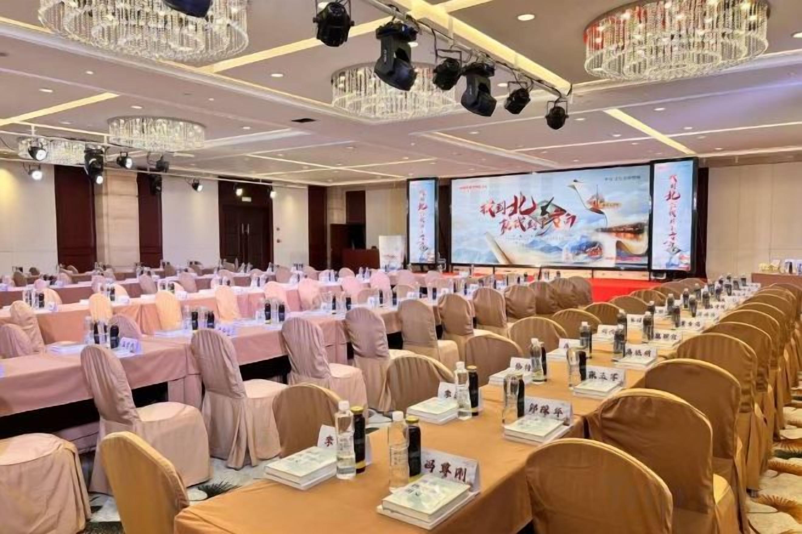 A conference room with rows of tables and chairs, a large screen, and a chandelier.