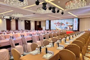 Un salón de conferencias con mesas y sillas dispuestas en filas, una pantalla grande y una araña de cristal.