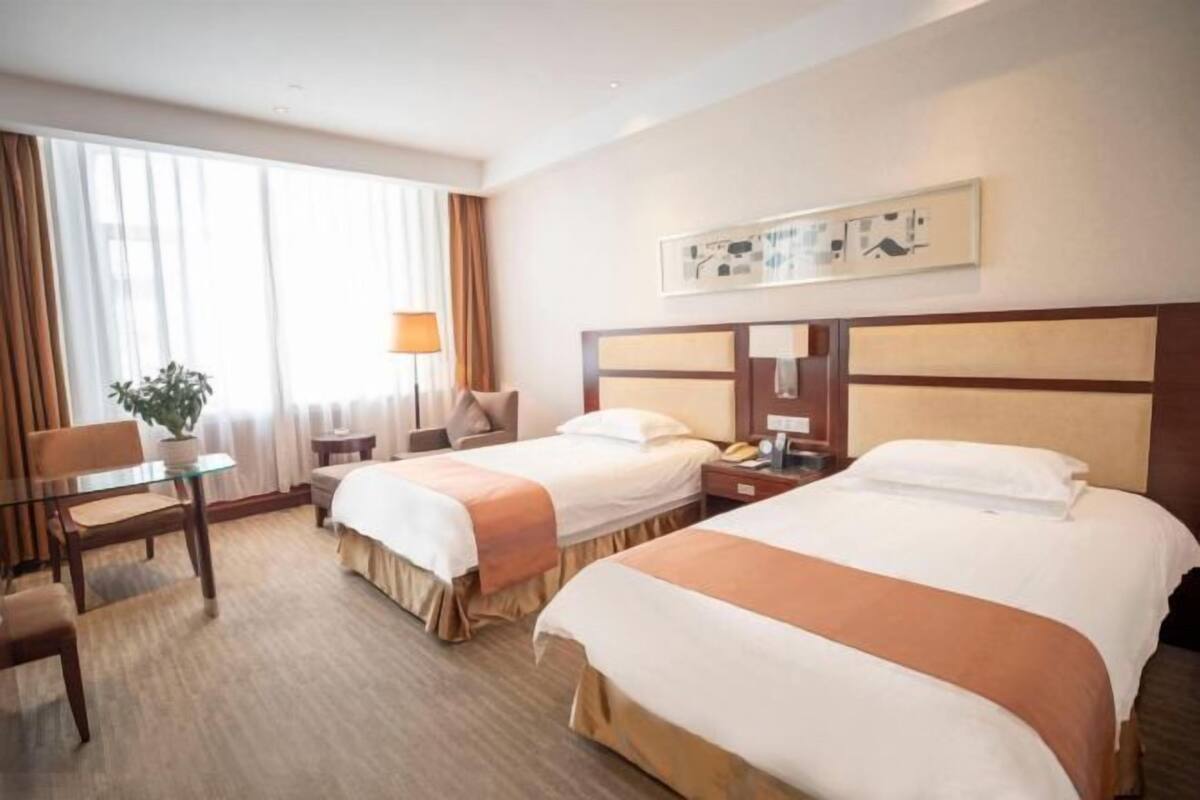 A hotel room with two beds, a desk, a chair, a lamp, and a window with curtains.