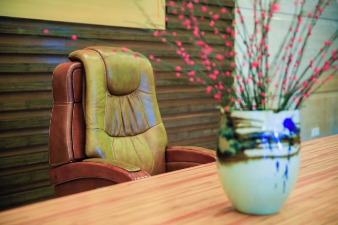 A leather chair with a cushioned backrest and a wooden table with a vase of pink flowers.