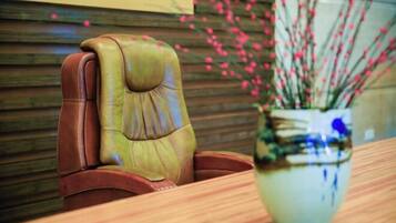 A leather chair with a cushioned backrest and a wooden table with a vase of pink flowers.