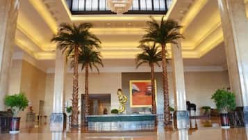 A spacious lobby with a reception desk, palm trees, and a modern chandelier.