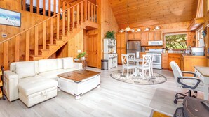 Une cabane en bois spacieuse comprenant un espace de vie, une cuisine et un escalier menant à une chambre à coucher située en mezzanine.
