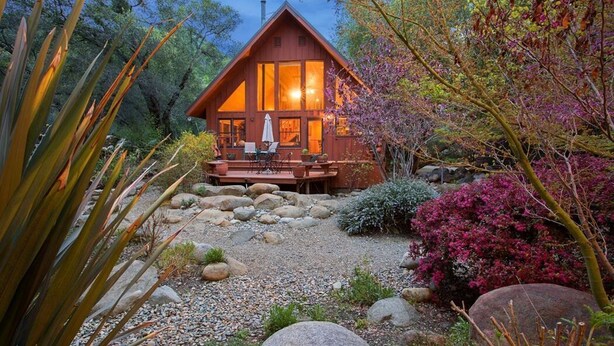 Une cabane en bois dotée d’une terrasse, entourée de rochers et de plantes.