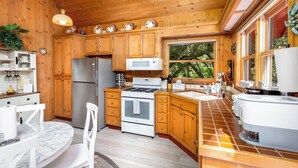 Une cuisine rustique, située dans une cabane en bois, équipée d’un réfrigérateur, d’une cuisinière, d’un four à micro-ondes et dotée d’une grande fenêtre.