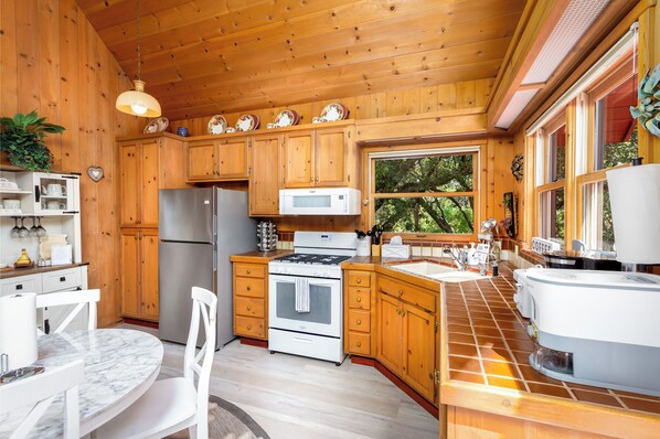 A wooden cabin kitchen with a refrigerator, stove, microwave, and a large window.