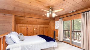 Une chambre dans une cabane en bois, avec un lit, un ventilateur de plafond et une porte-fenêtre coulissante donnant sur l’extérieur.