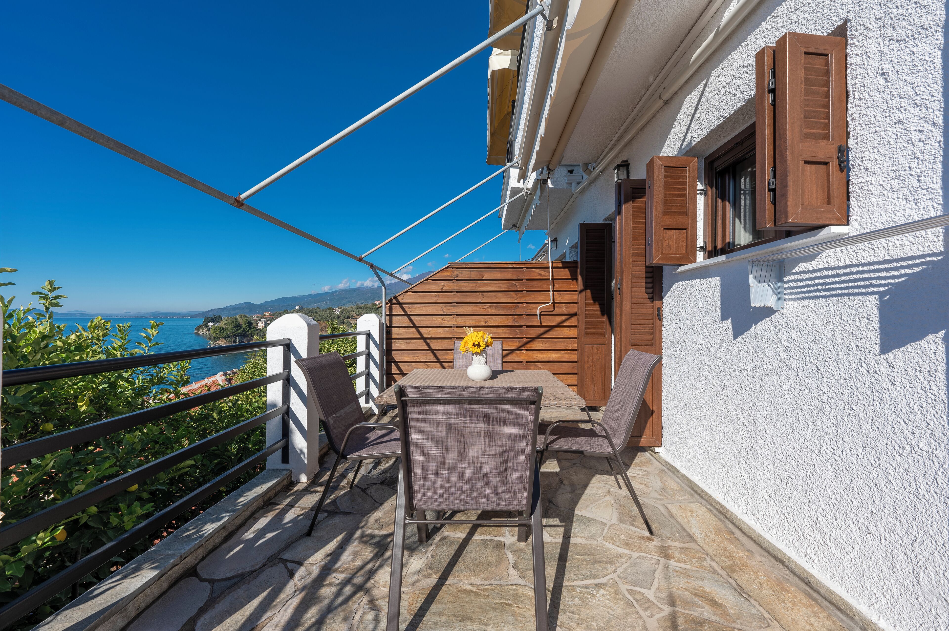 Un balcón con mesa y sillas, vista al mar y una pared blanca con textura.
