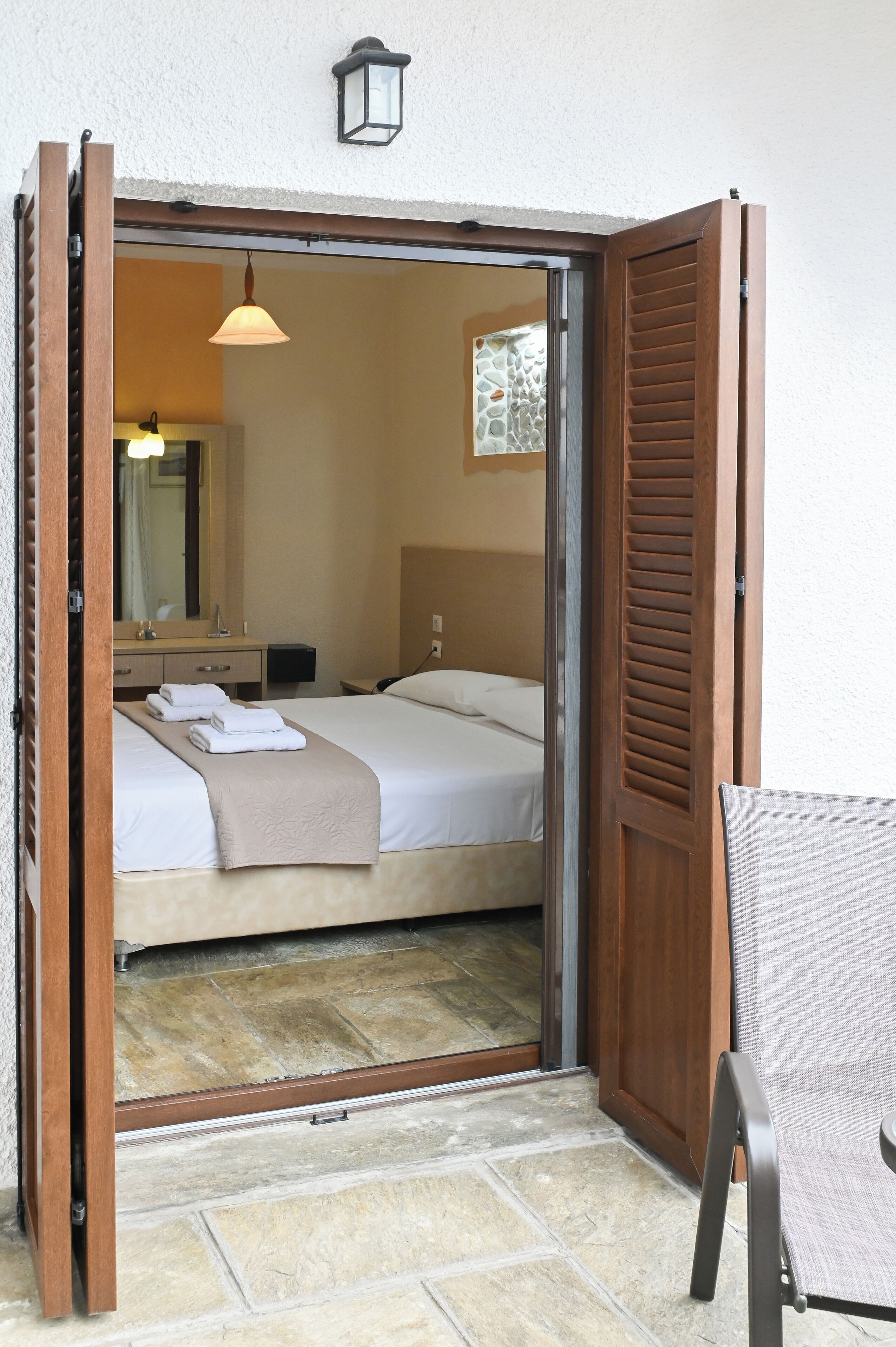 A hotel room with a bed, a chair, a table, a mirror, and a window.
