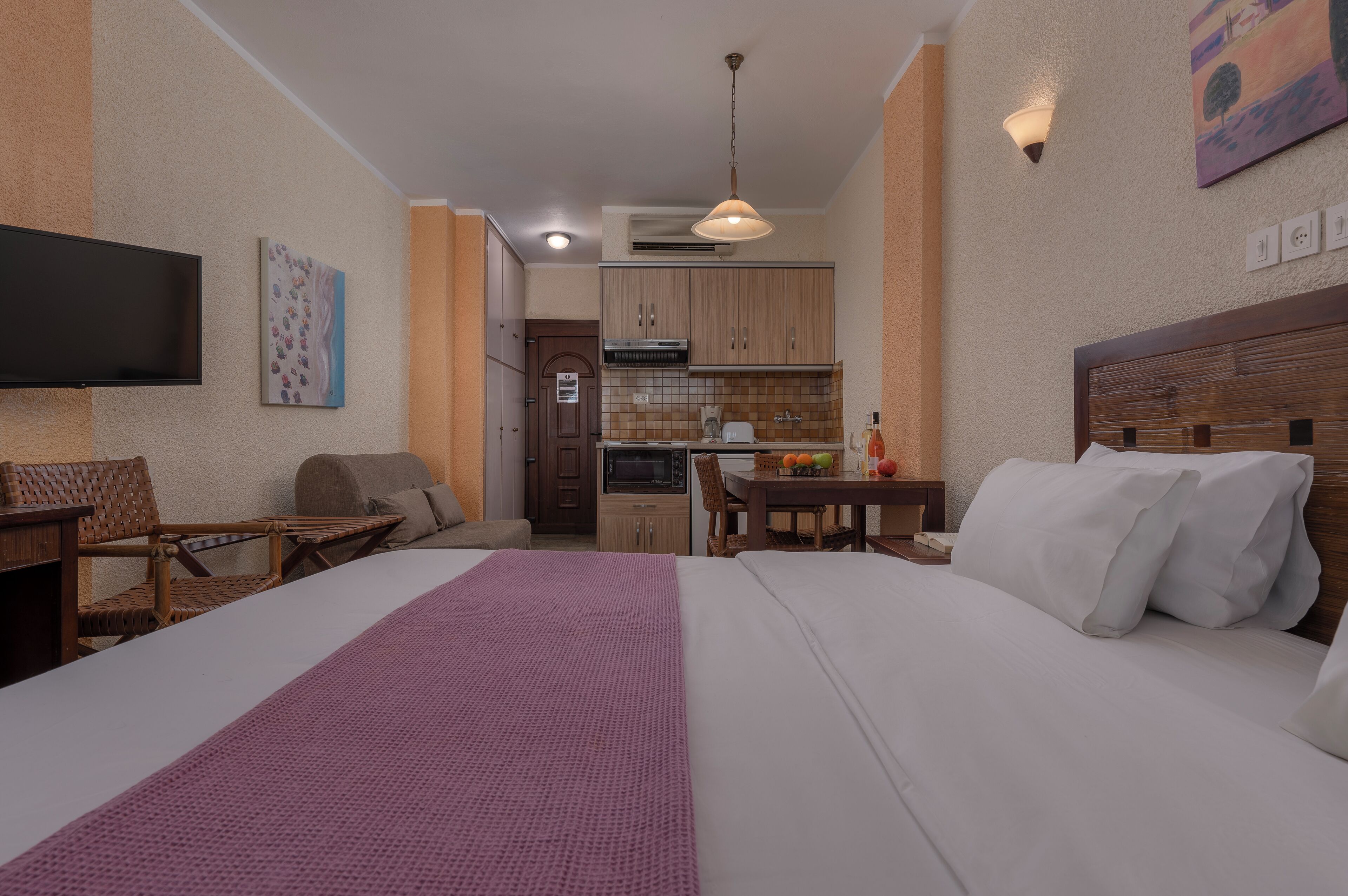 A hotel room with a bed, a desk, a chair, a TV, and a kitchenette.