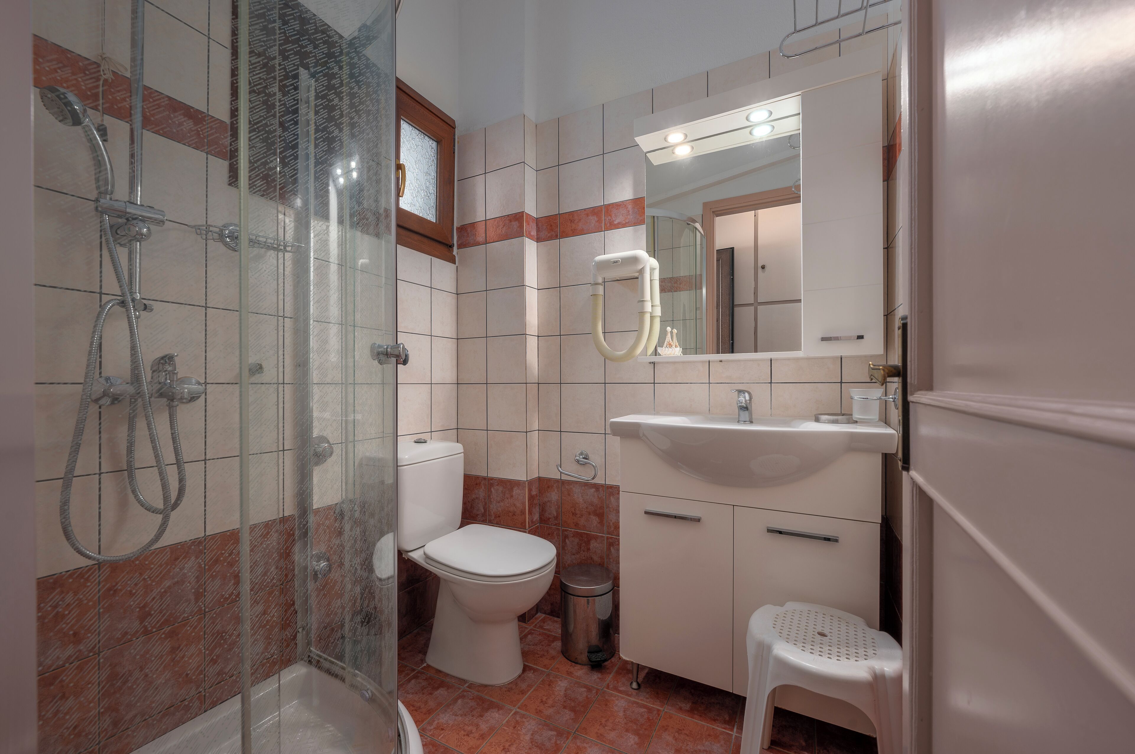 Ein Badezimmer mit einer Duschkabine, Toilette, Waschbecken und einem kleinen Hocker.