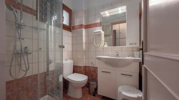 Ein Badezimmer mit einer Duschkabine, Toilette, Waschbecken und einem kleinen Hocker.